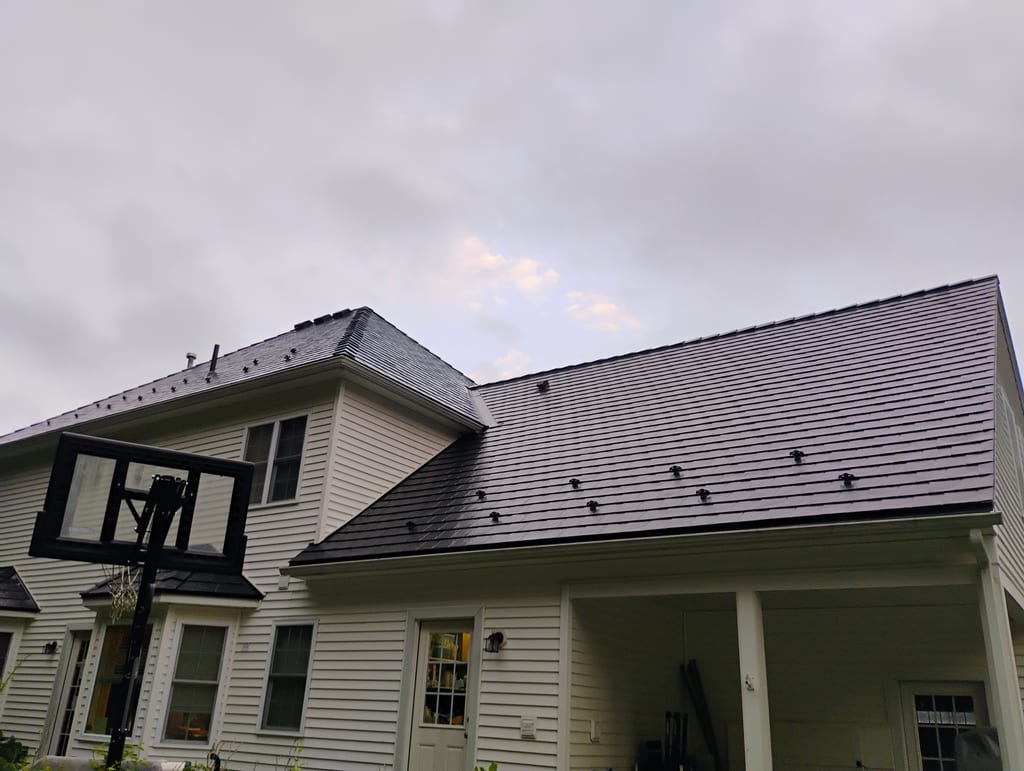 Two-story Colonial home with a complex black Interlock aluminum slate metal roof featuring snow guards, a dormer, and covered rear porch.