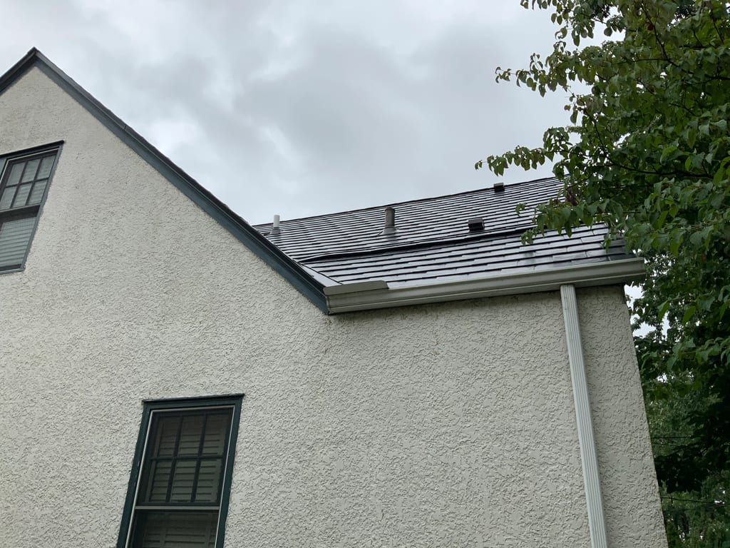 Deep Charcoal Interlock Slate aluminum roof on a white two-storey home with dormers among tall trees, Saint Paul, Minnesota