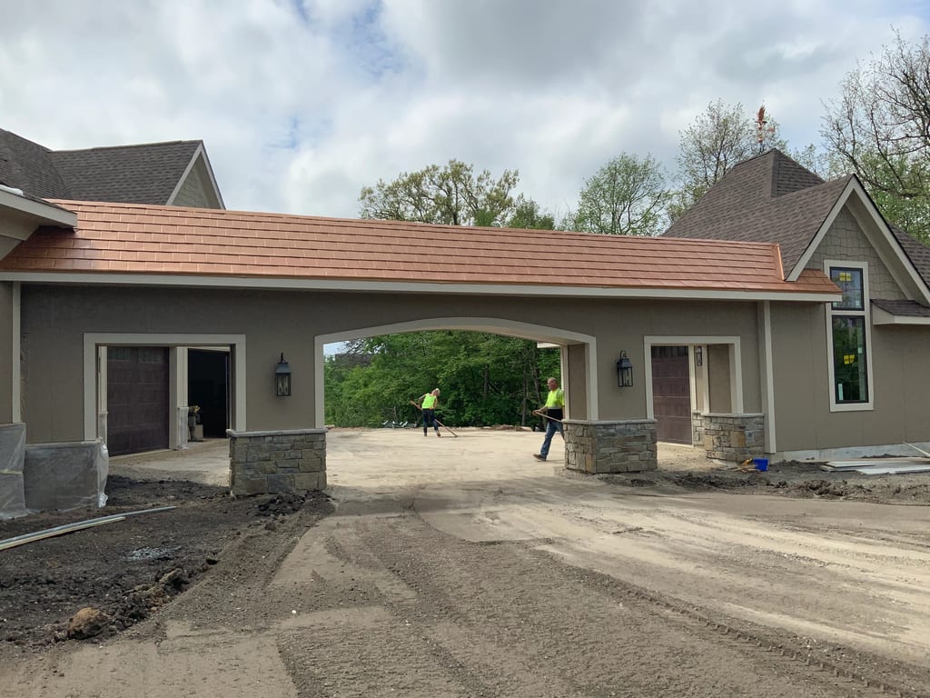 Copper Penny Interlock Slate aluminum roof being installed on a tan house with an arched entryway under construction near, Prior Lake, Minnesota