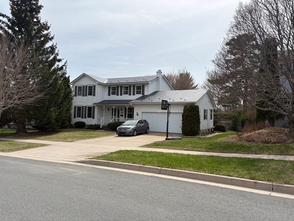 Deep Charcoal Interlock Slate aluminum roof on a white two-storey home with a metal roof among tall trees, Fredericton, New Brunswick