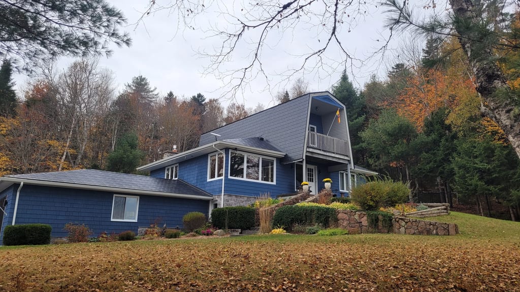 Black Interlock Slate aluminum roof on a blue one-storey cottage with dormers among tall pines, Utopia, New Brunswick