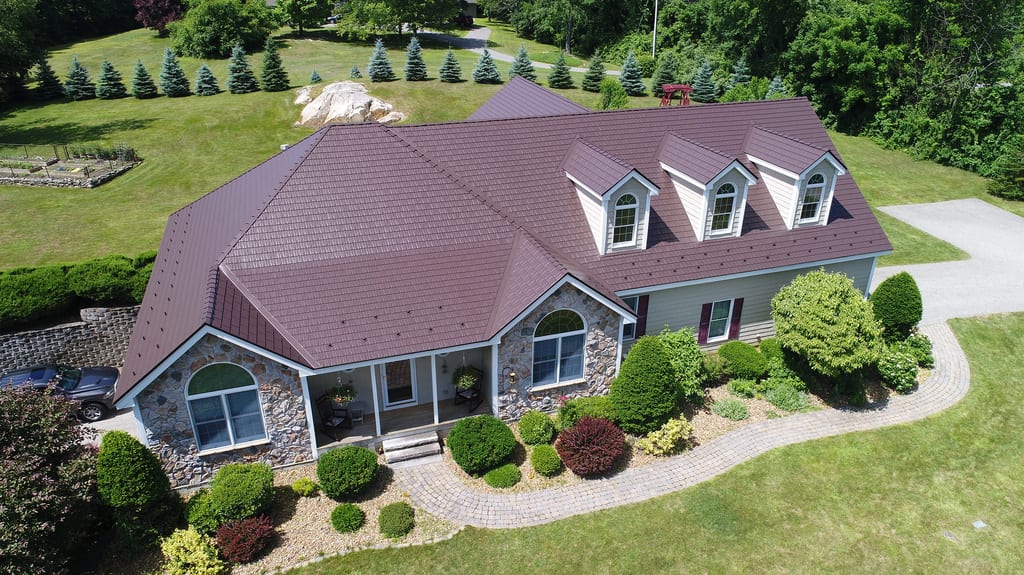 Aerial front view of a 1.5-story Colonial home in NH featuring an Interlock Colonial Brown cedar shingle metal roof with dormers and stone facade.