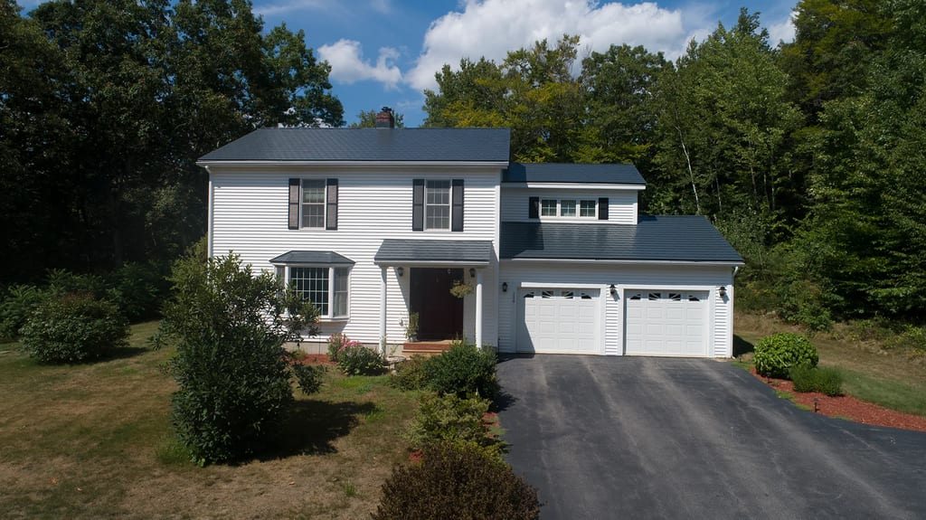 Charcoal Grey Interlock Slate aluminum roof on a white two-storey colonial home with dormers in a forest, Webster, New Hampshire