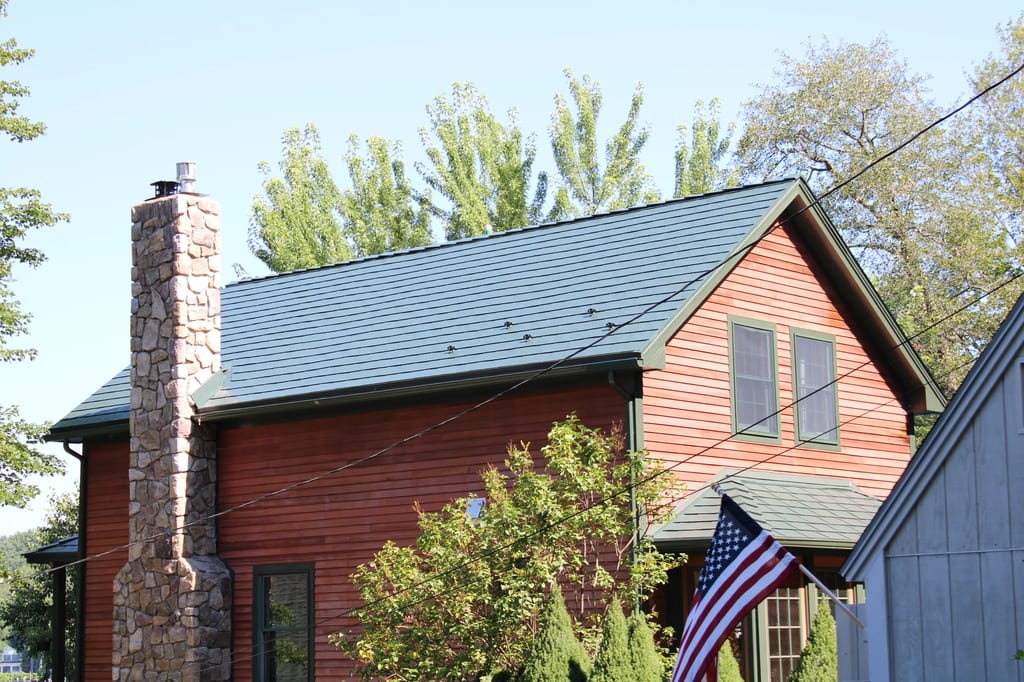 Hunter Green Interlock Slate aluminum roof on a red colonial home with dormers among tall trees, Pelham, New Hampshire