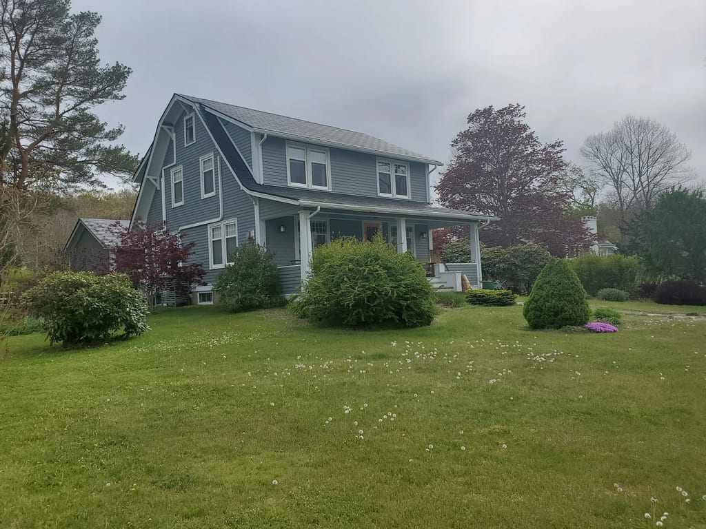 Black Interlock Slate aluminum roof on a green two-storey home with dormers in a lush green, Mahone Bay, Nova Scotia