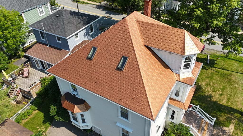 Aged Copper Interlock Slate aluminum roof on a white two-storey home with dormers among tall trees, Lunenburg, Nova Scotia