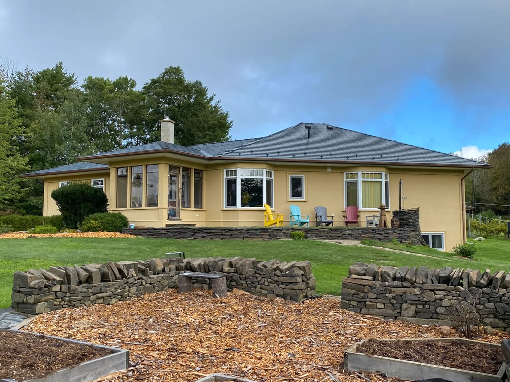 Deep Charcoal Interlock Slate aluminum roof on a yellow one-storey home with a chimney in a forested rural, Bridgewater, Nova Scotia