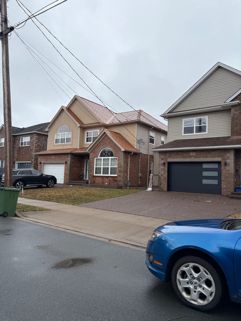 Copper Penny Interlock Slate aluminum roof on a tan two-storey home with dormers among tall pines, Dartmouth, Nova Scotia
