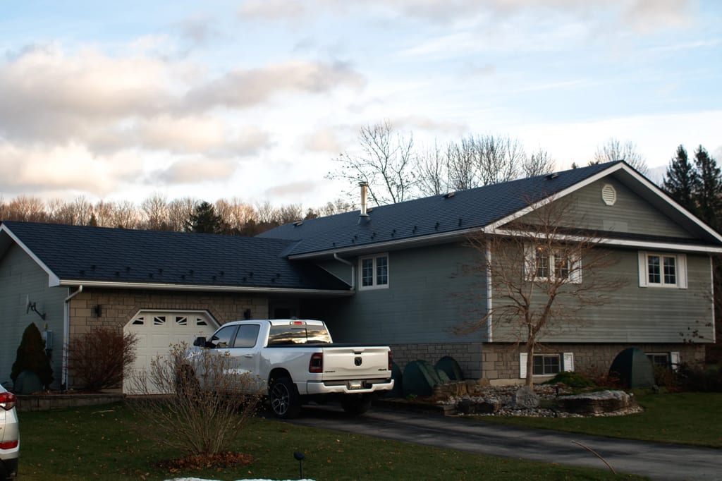 Black Interlock Slate aluminum roof on a two-storey home with a metal roof among tall trees, Wiarton, Ontario