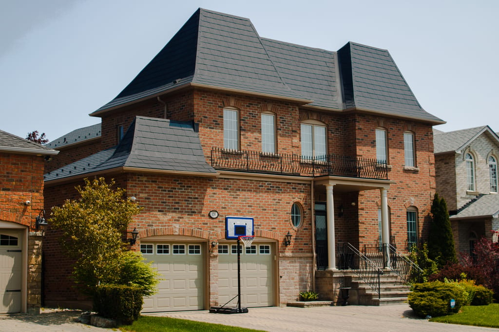 Two-storey brick Colonial home in Woodbridge ON with a complex multi-hip black Interlock aluminum slate metal roof and prominent Mansard-style lower sections.
