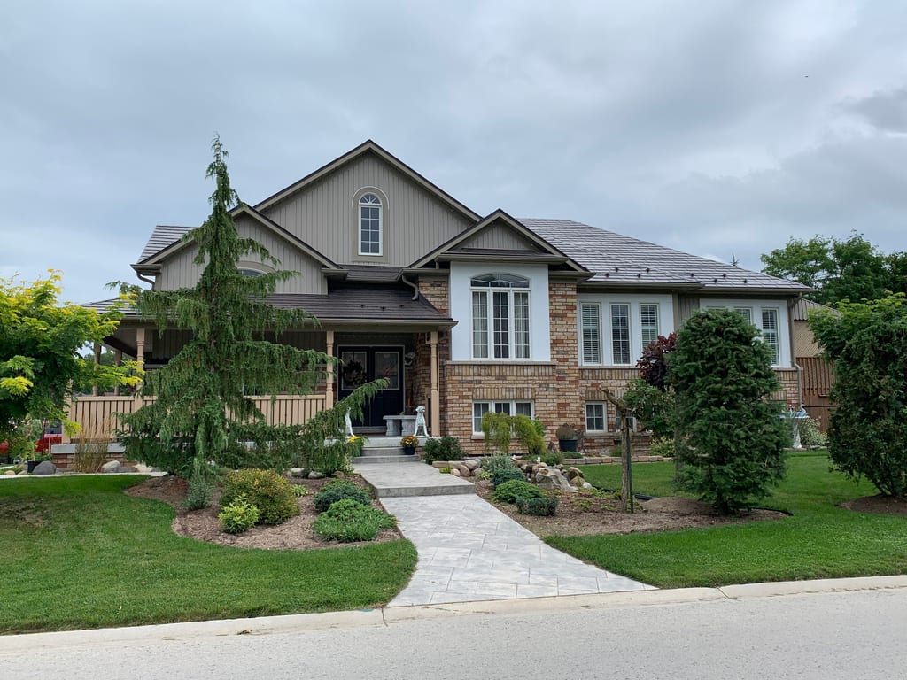 Craftsman-style brick home in Wasaga Beach with Interlock Tudor Brown aluminum slate metal roofing, multi-hip complex roofline, and landscaped front yard.