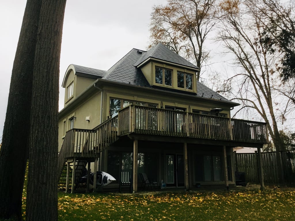 Rear elevation of a 3-storey Victorian home in Orillia ON featuring black Interlock aluminum slate roofing with a central turret, dormer, and large elevated wood deck.