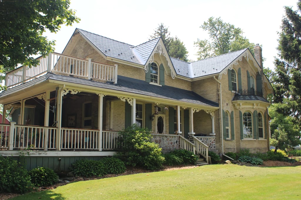 Deep Charcoal Interlock Cedar Shingle aluminum roof on a tan two-storey Victorian home with dormers among tall, Thorndale, Ontario