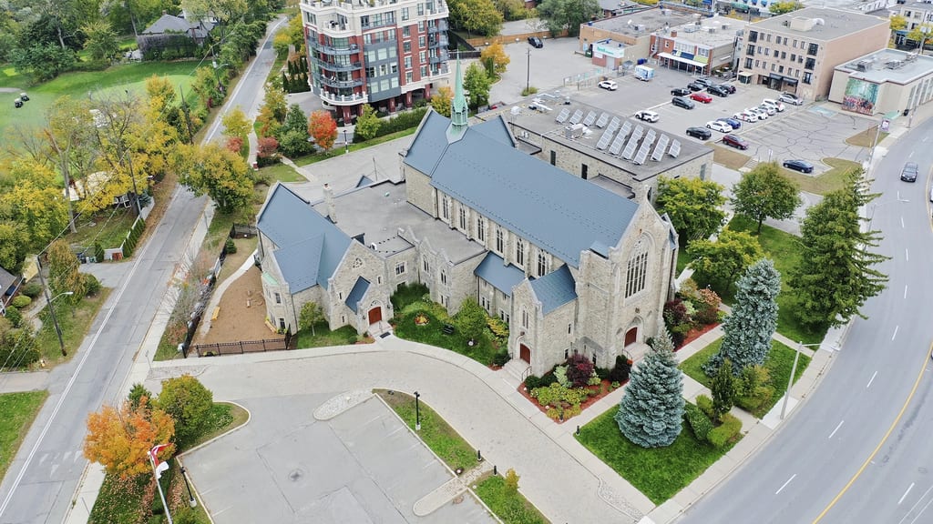 Aerial view of a historic stone church in Toronto with deep charcoal Interlock aluminum slate roofing featuring complex multi-gable geometry and solar panels.
