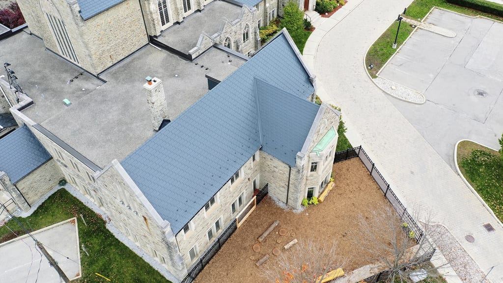 Aerial view of a deep charcoal Interlock aluminum slate metal roof on a historic stone church in Toronto, featuring complex multi-gable geometry and a stone chimney.