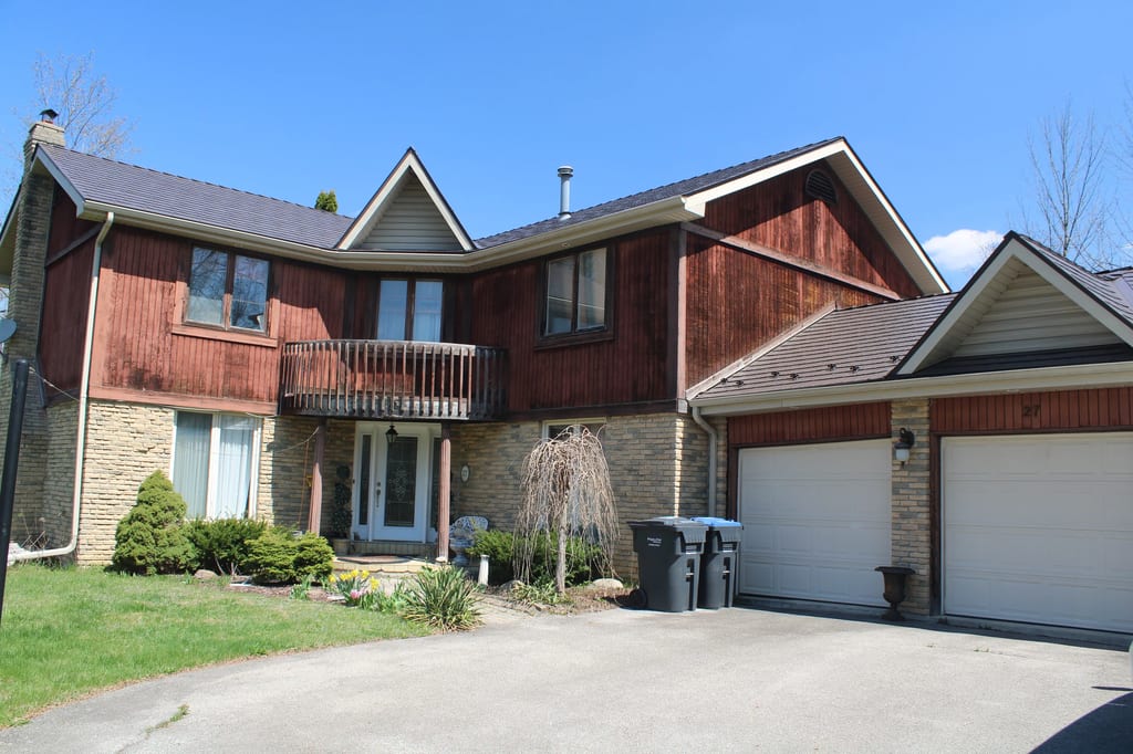 Tudor Brown Interlock Cedar Shingle aluminum roof on a brown two-storey home with dormers among tall pines, Caledon, Ontario