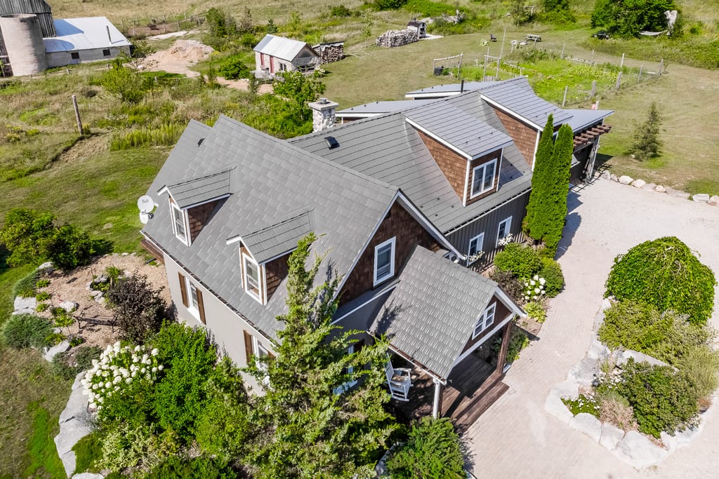 Aerial view of a complex multi-hip Interlock aluminum cedar shingle roof in Weathered finish on a rural Craftsman-style two-storey home in Midland, ON.