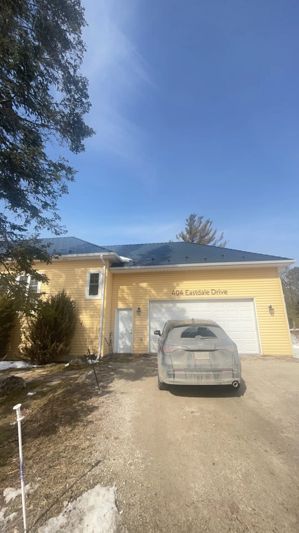 Deep Charcoal Interlock Cedar Shingle aluminum roof on a yellow home with a metal roof among tall pines, Wasaga Beach, Ontario
