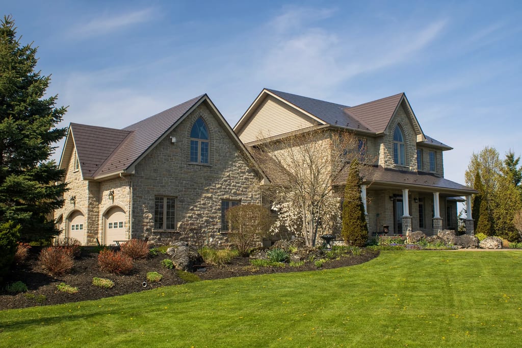 Large two-storey stone estate home in Ariss ON featuring Interlock Tudor Brown aluminum slate metal roofing with complex multi-gable steep roof profile.