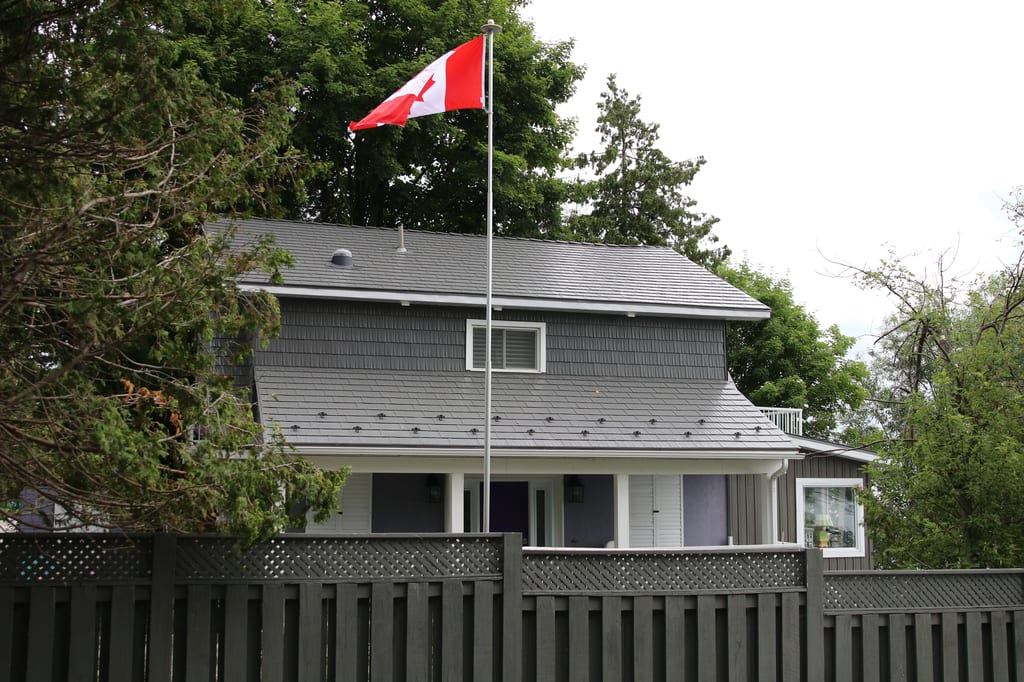 Musket Grey Interlock Cedar Shingle aluminum roof on a grey two-storey home with a metal roof among tall trees, Severn, Ontario