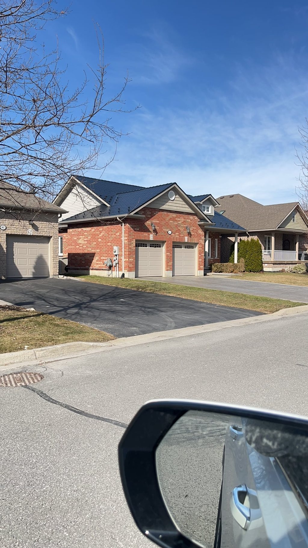 Street-view of a brick semi-detached home in Cobourg, ON featuring a black Interlock aluminum slate metal roof with multi-hip profile.