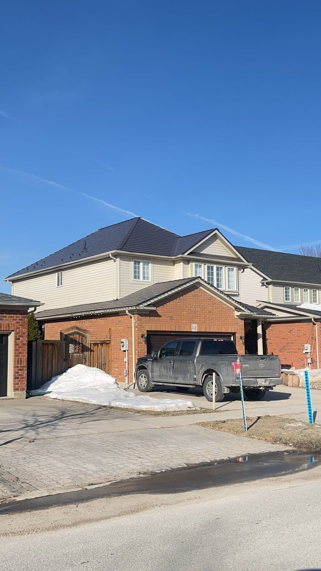 Two-storey brick home in Collingwood, ON with a complex hip roof clad in Interlock Tudor Brown aluminum slate roofing under a clear blue winter sky.