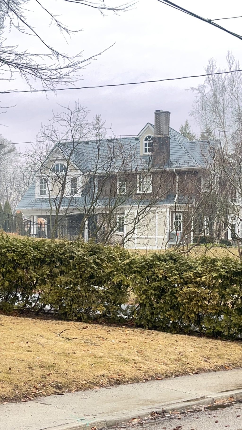 Two-storey colonial brick home in Burlington ON with steep deep charcoal Interlock aluminum slate roof, twin dormers, and brick chimney, viewed from street.