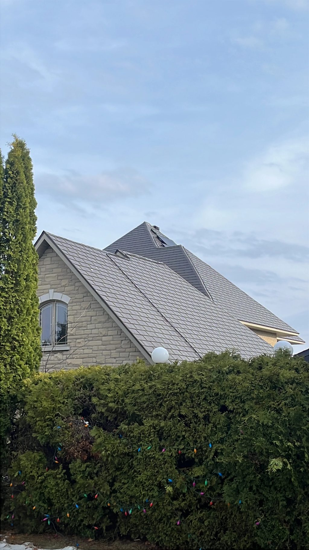 Tudor Brown Interlock Slate aluminum roof on a brown two-storey Tudor home with dormers among tall pines, Sudbury, Ontario