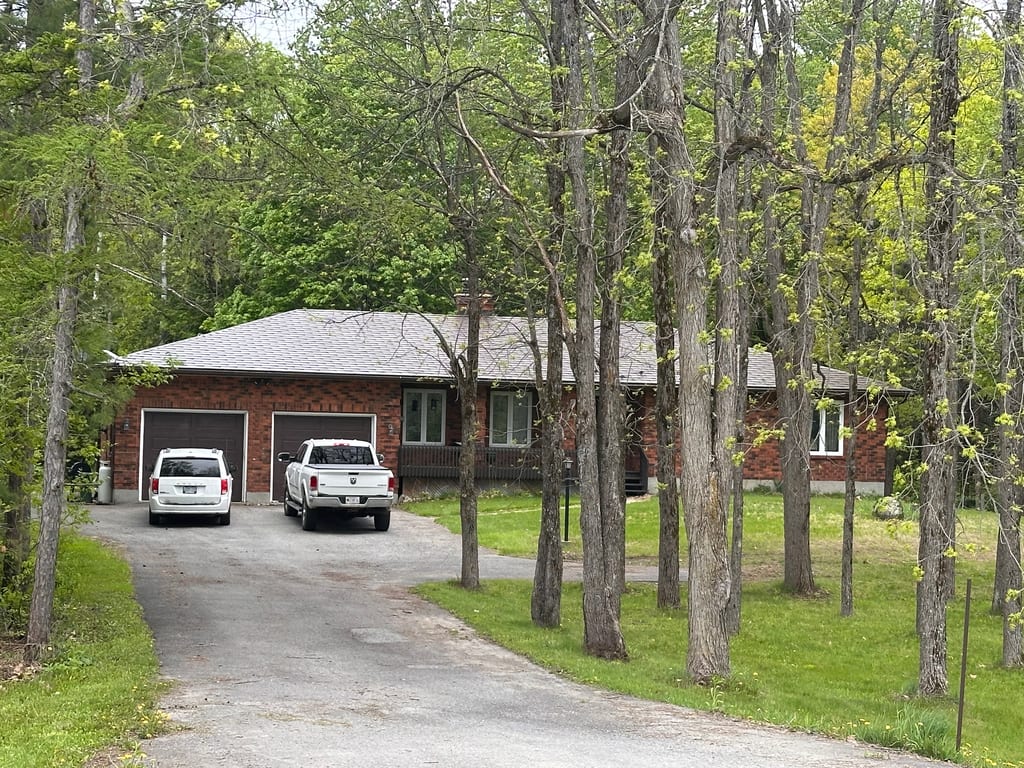 Single-storey brick ranch home in Richmond ON with Colonial Brown Interlock aluminum shingle roof, hip profile, viewed through mature trees from front-left.