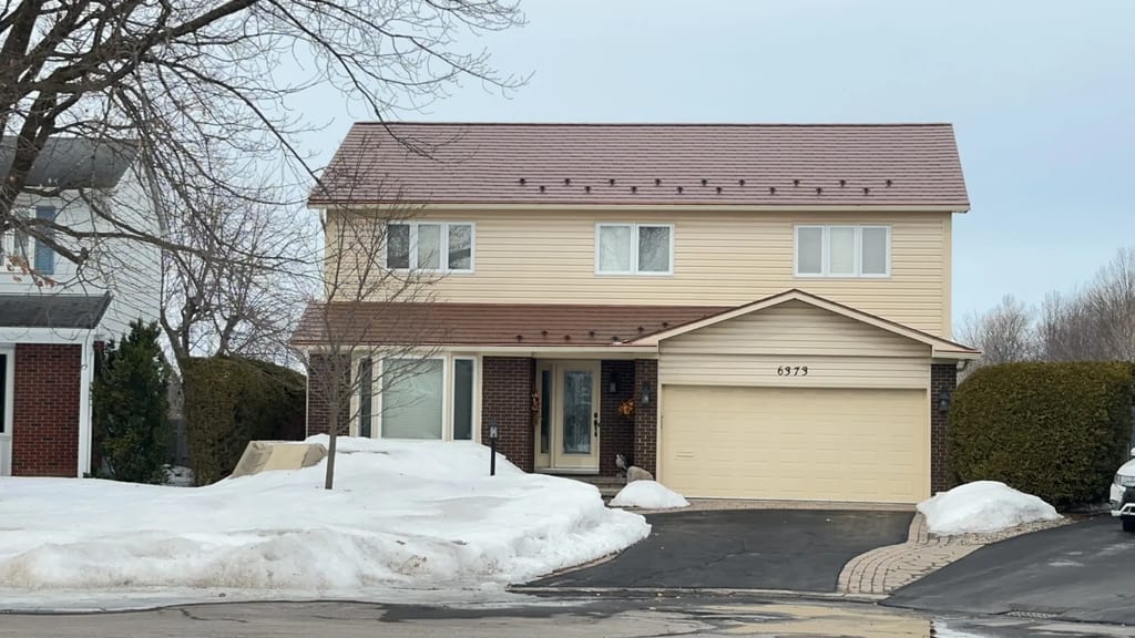 Two-storey colonial-style home in Orleans ON with Interlock aged copper aluminum shingle metal roof, snow guards visible along eaves, winter setting.