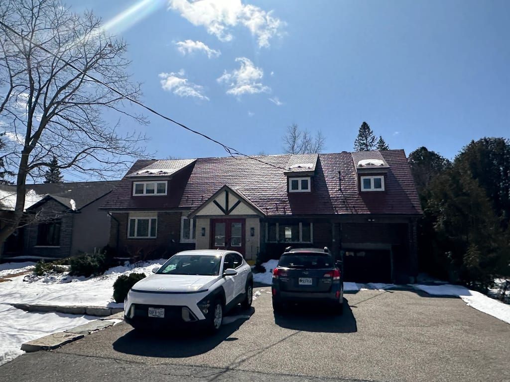 Tile Red Interlock Shingle aluminum roof on a red two-storey home with dormers among tall pines, Stittsville, Ontario