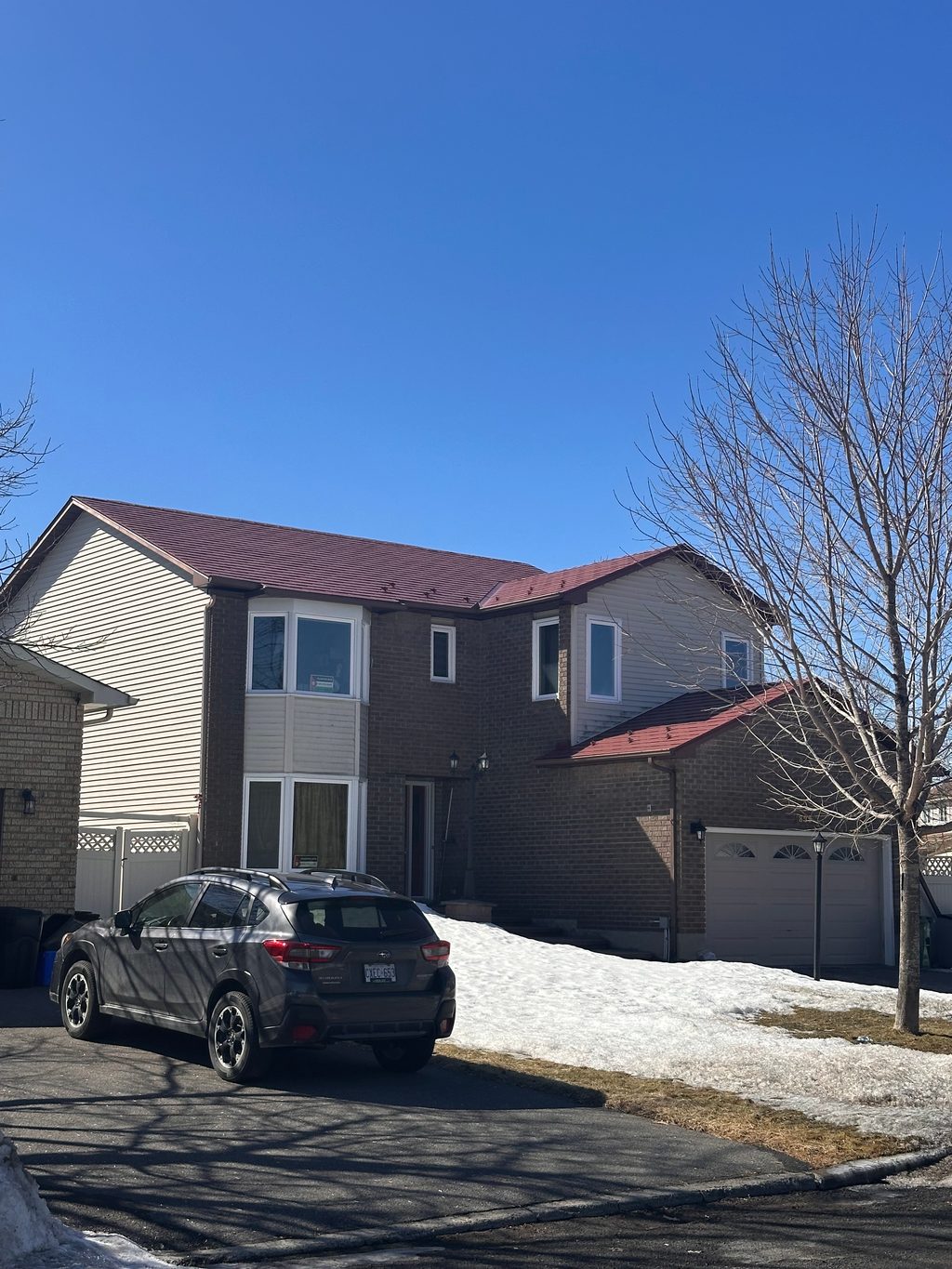Two-storey brick suburban home in Orleans ON with Interlock Tile Red aluminum shingle metal roofing on a multi-hip complex roof, clear winter sky.