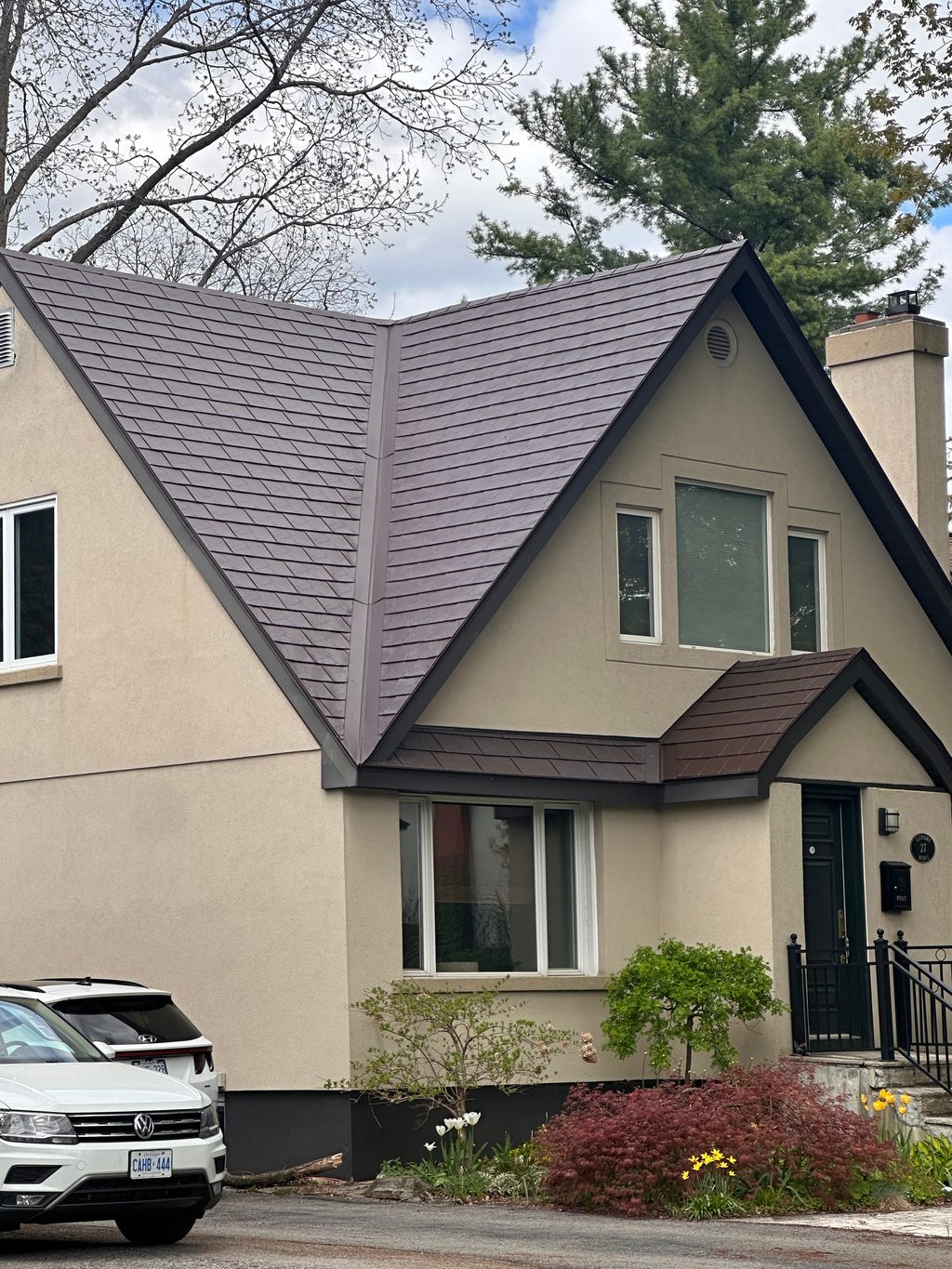 Two-storey Tudor-style home with a complex steep-pitched Colonial Brown Interlock aluminum slate roof featuring dormers, valleys, and a chimney.
