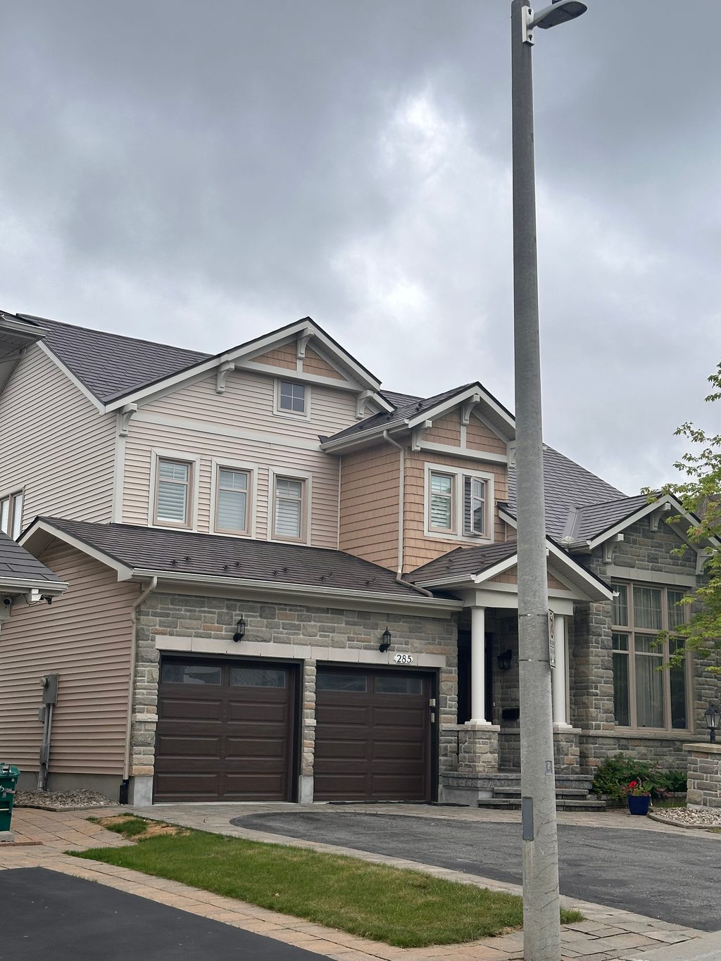 Two-storey Craftsman home at 285 with Interlock Tudor Brown aluminum slate roofing, multi-plane gabled roof, stone facade, and double garage.