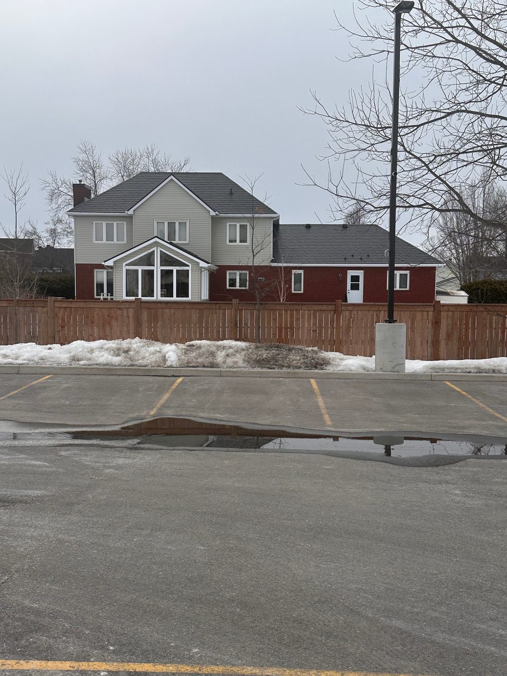 Rear elevation of a two-storey suburban home in Navan, ON with dark slate-profile Interlock aluminum roofing, red brick lower level, and gabled sunroom addition.