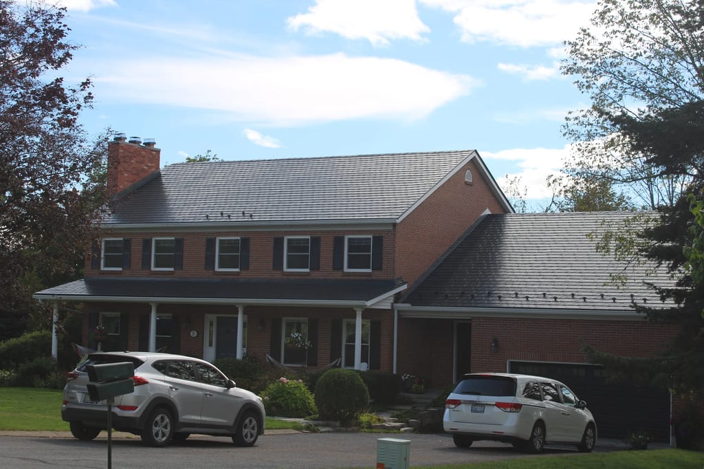 Black Interlock Slate aluminum roof on a red brick home with a metal roof among green trees, Kingston, Ontario