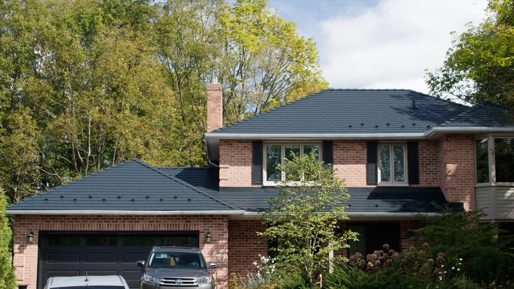 Two-storey brick Colonial home in Kingston, ON featuring a complex black Interlock aluminum slate metal roof with snow guards and brick chimney.
