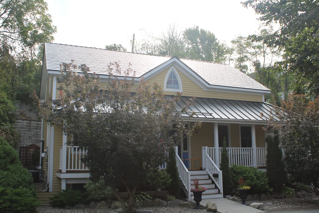 Black Interlock Slate aluminum roof on a yellow single-storey cottage among tall trees, Kingston, Ontario