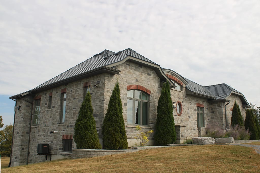 Deep Charcoal Interlock Slate aluminum roof on a grey stone house with a slate roof and a lawn, Picton, Ontario