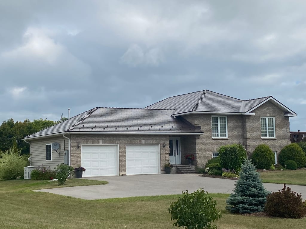 Front-left view of a rural Ontario home with Interlock Tudor Brown cedar shingle aluminum metal roofing on a multi-hip complex roofline over brick exterior.