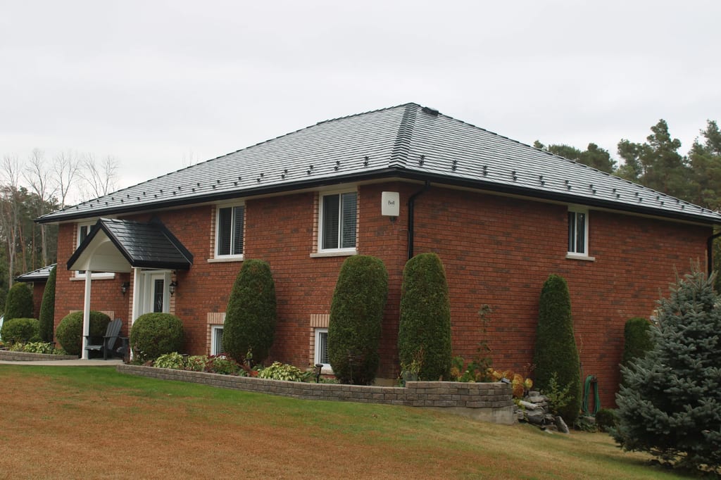 Black Interlock Slate aluminum roof on a red brick home with a metal roof and bushes in a rural, Carrying Place, Ontario