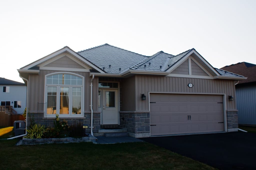 Single-family ranch-style home in Belleville ON with Interlock Tudor Brown aluminum slate metal roofing featuring multi-hip complex roof profile and stone accent base.