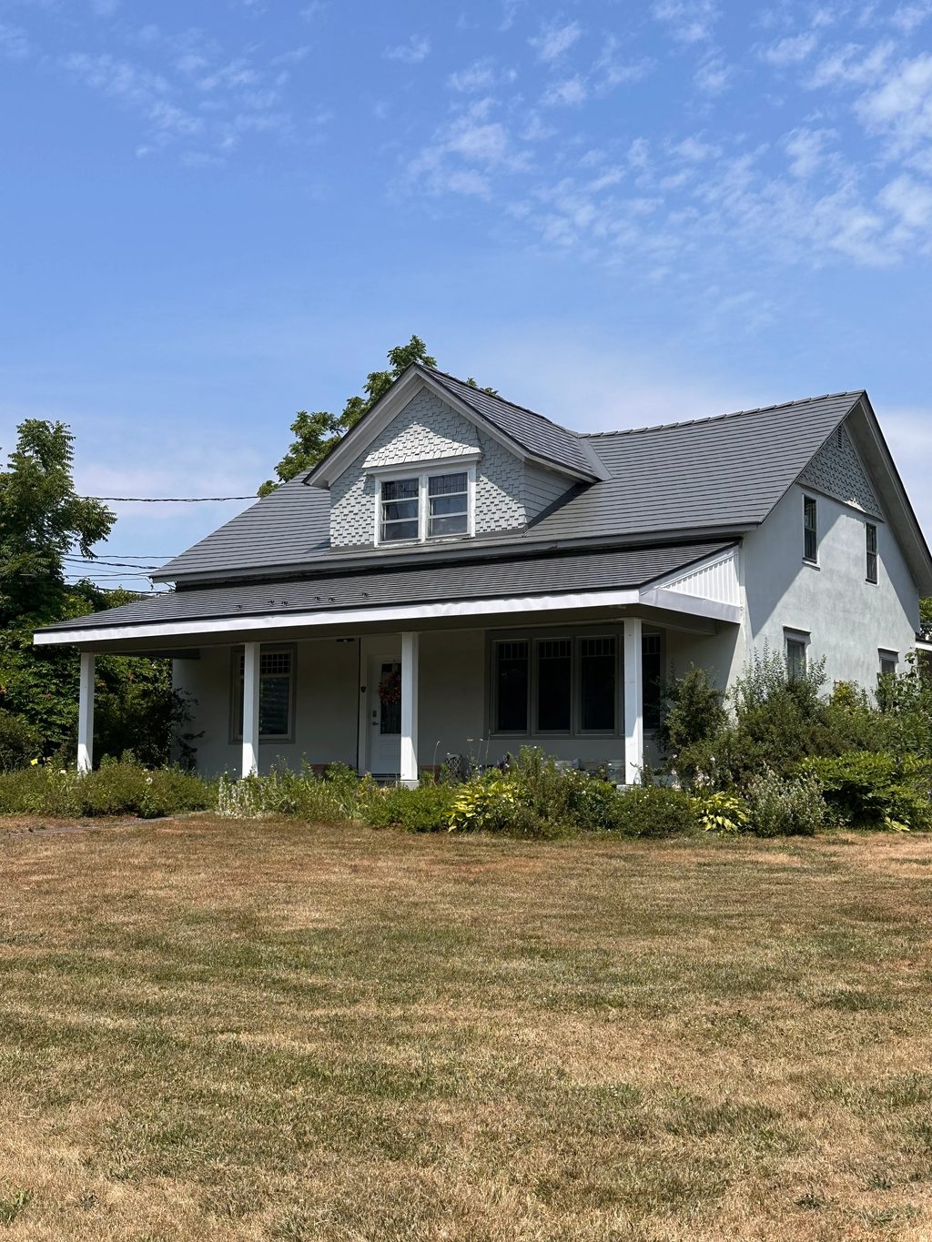 Musket Grey Interlock Slate aluminum roof on a grey two-storey home with dormers among tall pines, Bloomfield, Ontario
