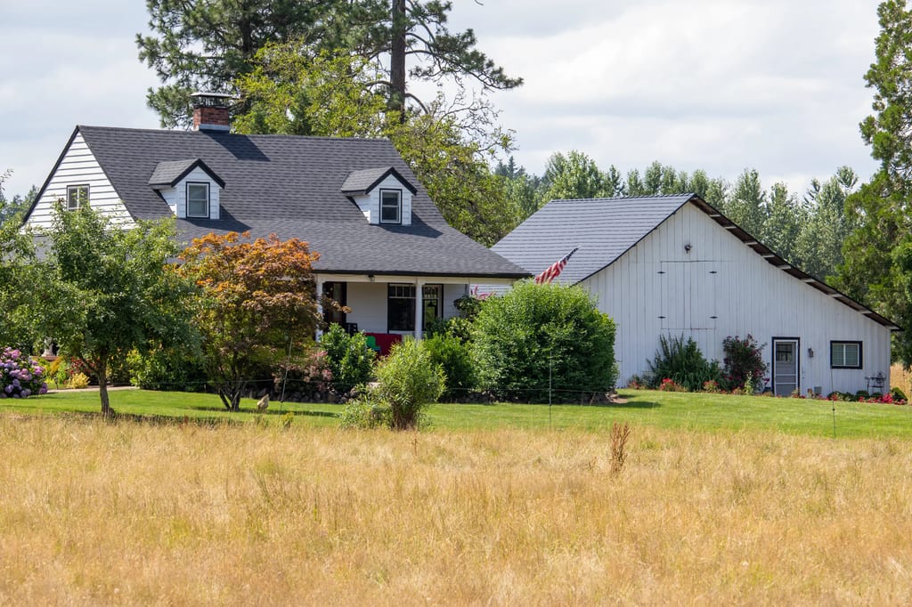 Black Interlock Shingle aluminum roof on a white house with a gray roof among tall trees, Hillsboro, Oregon