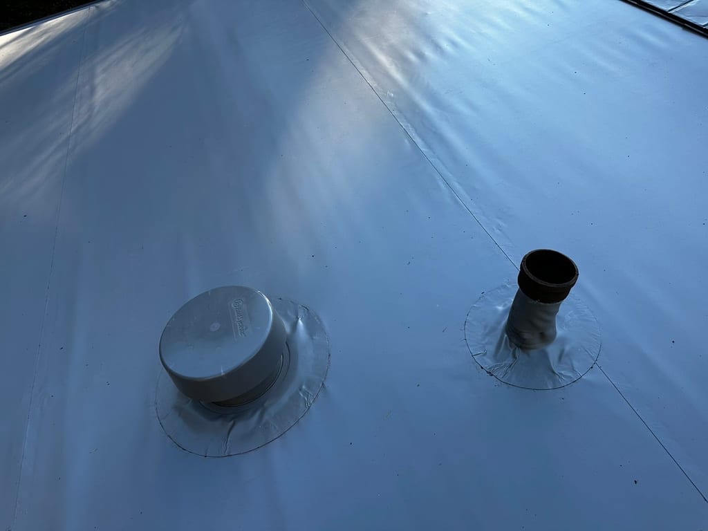 Close-up of a white TPO or membrane flat roof showing two penetrations: a capped roof vent and an open vent pipe with flashing boots.