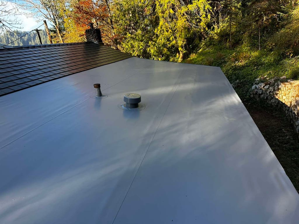 Low-slope Interlock aluminum slate roof in black on a forested mountain home in Alsea, OR, with vent pipe and roof louver penetrations.
