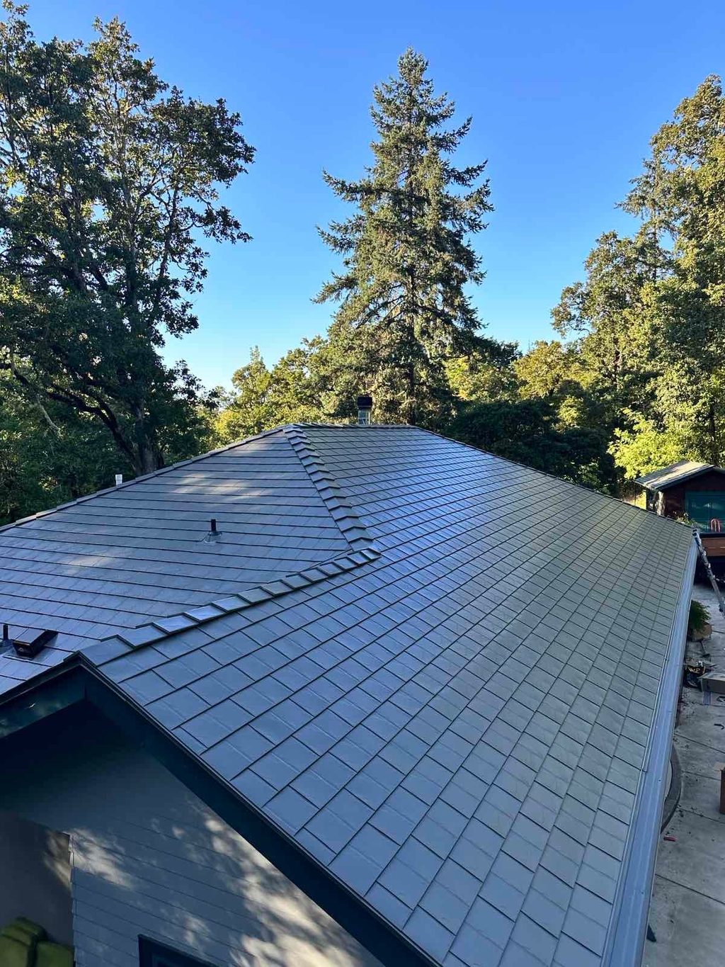 Aerial overview of a complex multi-hip Interlock aluminum slate roof in Musket Grey on a forested single-family home in Eugene, OR.