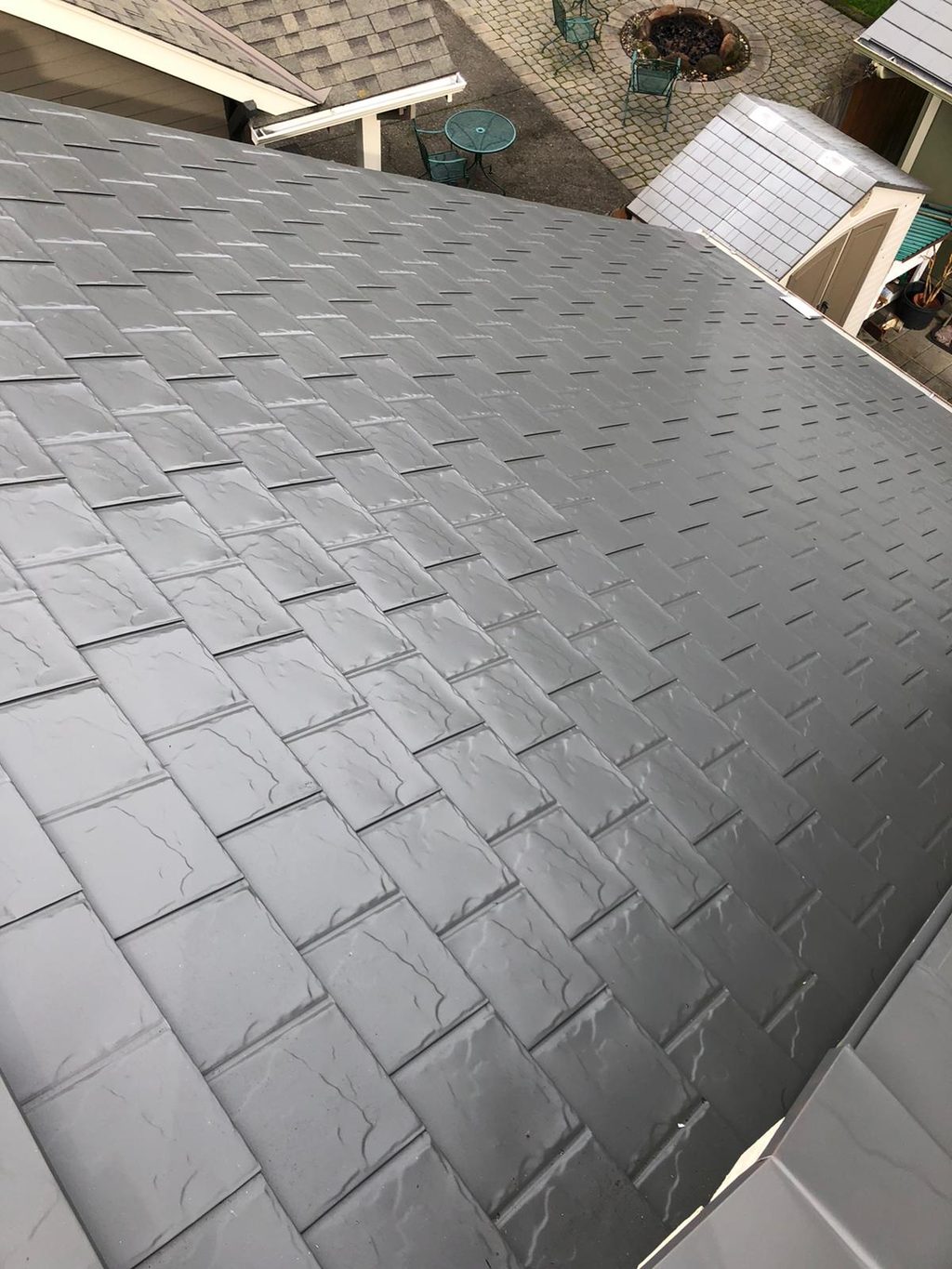 Close aerial view of Interlock aluminum slate roofing in Musket Grey on a residential hip roof in Scappoose, OR, showing wet tile texture detail.