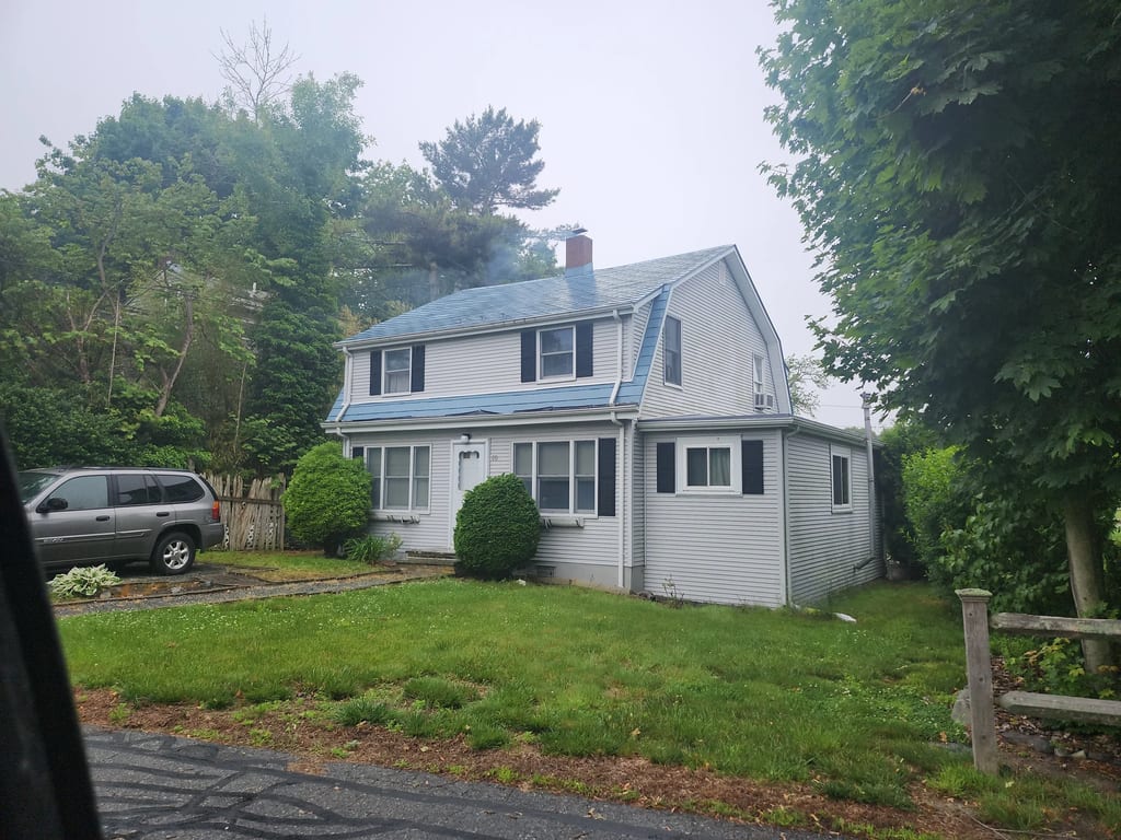 Charcoal Grey Interlock IB Membrane aluminum roof on a white two-storey home with dormers among tall trees, Portsmouth, Rhode Island
