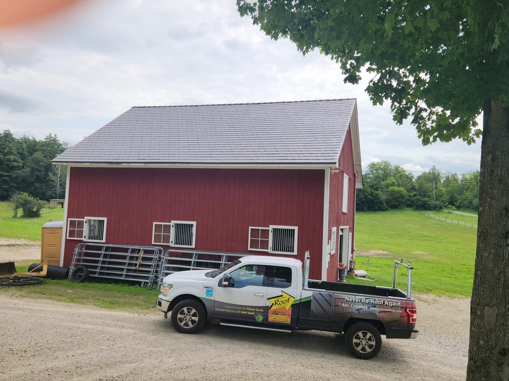 Red Vermont barn with a freshly installed Interlock aluminum slate roof in Tudor Brown, simple gable profile, photographed from front-left elevation.